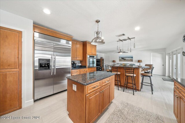 kitchen featuring a kitchen island, dark stone countertops, appliances with stainless steel finishes, and hanging light fixtures