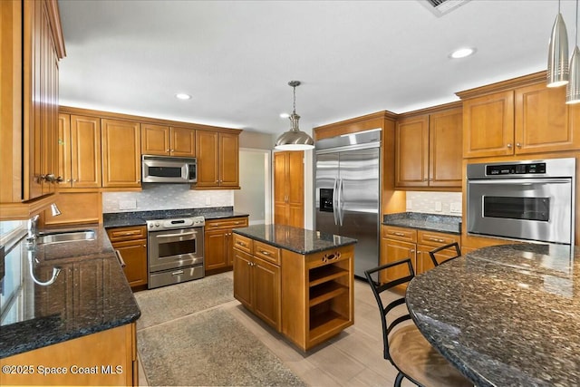 kitchen featuring sink, appliances with stainless steel finishes, a kitchen island, pendant lighting, and dark stone counters