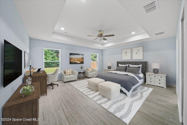 bedroom featuring ceiling fan, a tray ceiling, and multiple windows