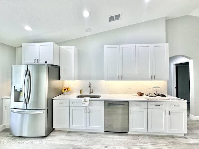 kitchen with sink, vaulted ceiling, stainless steel fridge, black dishwasher, and white cabinets