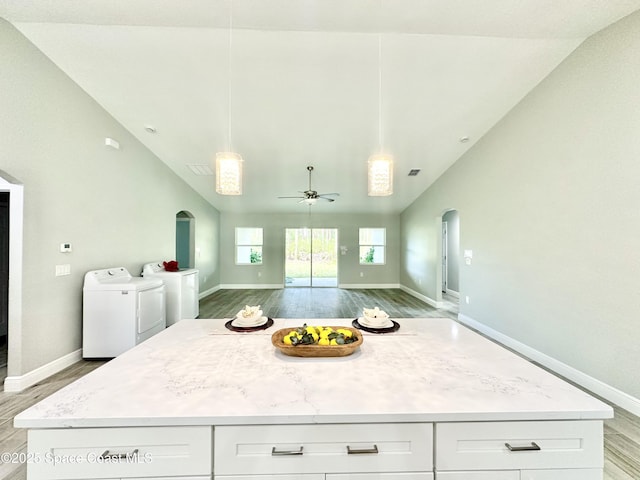 kitchen featuring washing machine and clothes dryer, lofted ceiling, hanging light fixtures, ceiling fan, and white cabinets