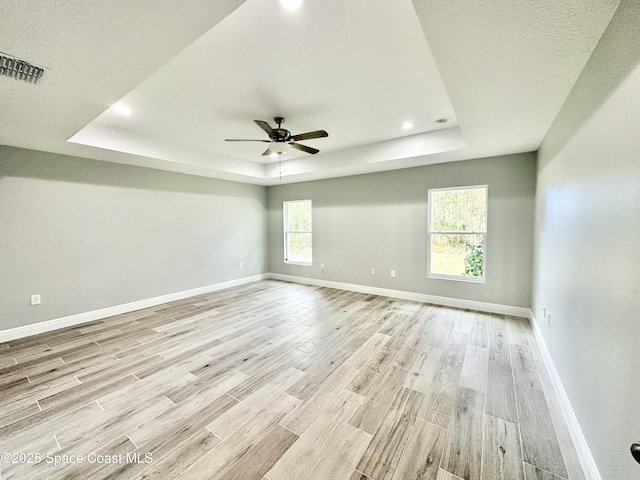 spare room featuring a tray ceiling, light hardwood / wood-style flooring, and ceiling fan