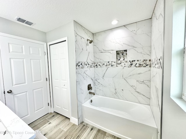 bathroom featuring a textured ceiling and tiled shower / bath