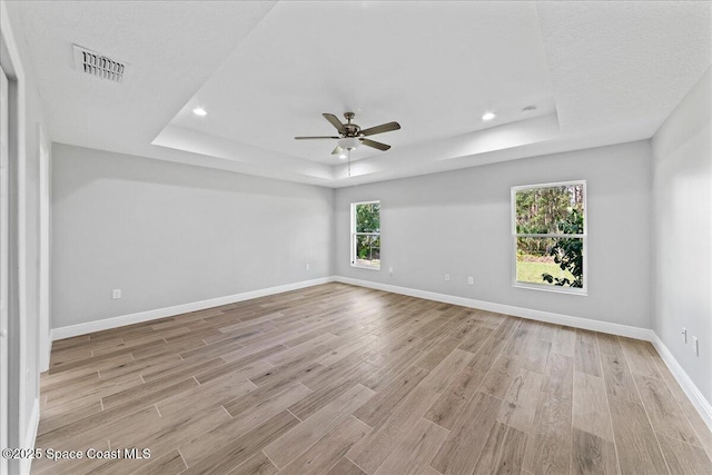 spare room with a tray ceiling, light wood-type flooring, visible vents, and baseboards