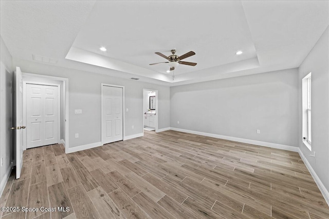 unfurnished bedroom with light wood-style floors, a raised ceiling, connected bathroom, and baseboards