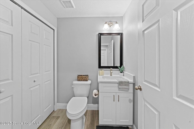 half bath with visible vents, toilet, wood finished floors, vanity, and a closet