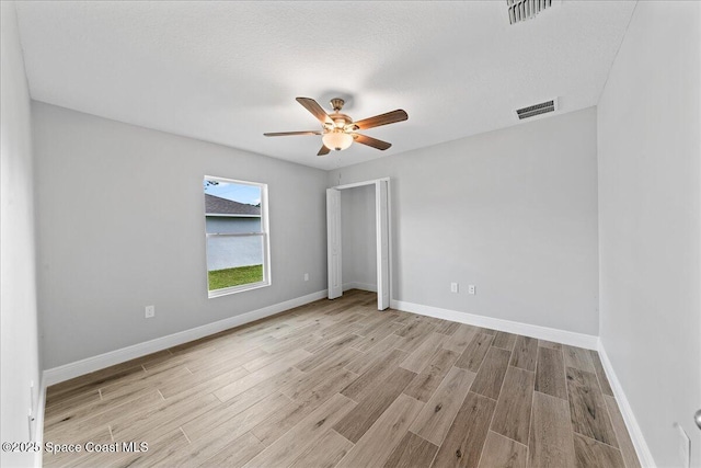 empty room featuring light wood finished floors, a ceiling fan, visible vents, and baseboards