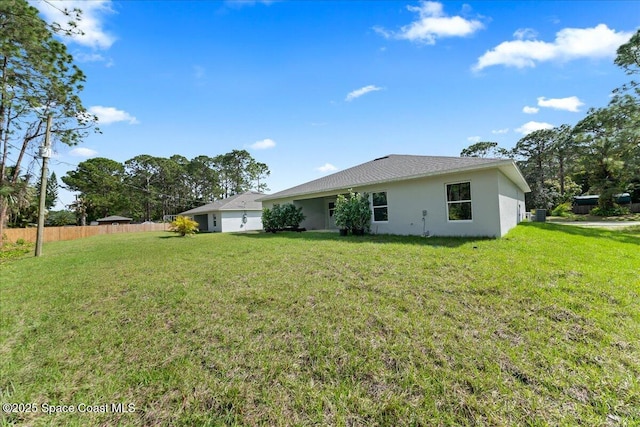 rear view of property with stucco siding, fence, and a yard