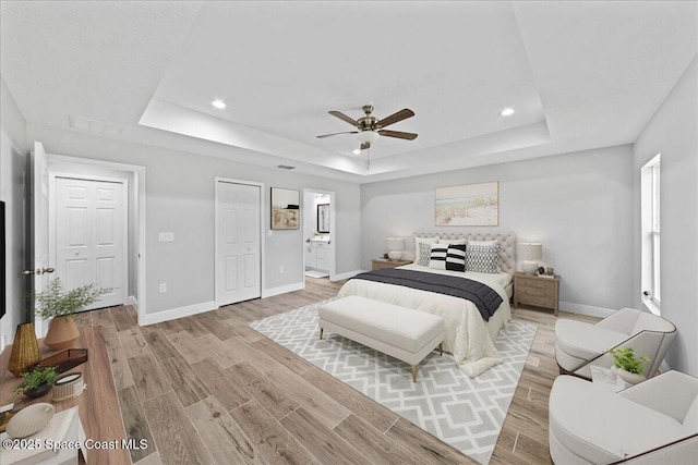 bedroom with light wood-style floors, a tray ceiling, visible vents, and baseboards