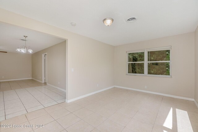 spare room with a notable chandelier and light tile patterned flooring