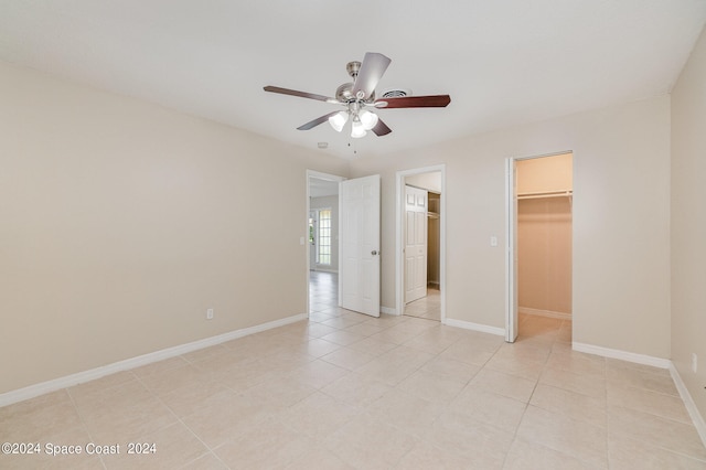 unfurnished bedroom featuring ceiling fan, a closet, light tile patterned floors, and a walk in closet