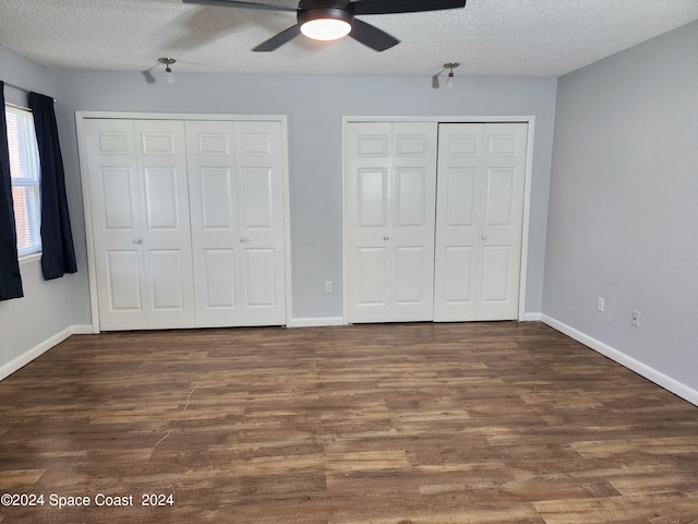 unfurnished bedroom featuring two closets, ceiling fan, dark hardwood / wood-style floors, and a textured ceiling