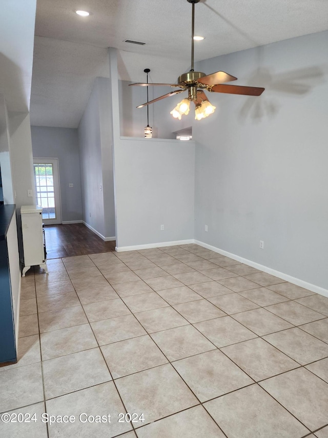 interior space with a textured ceiling, light tile patterned flooring, vaulted ceiling, and ceiling fan