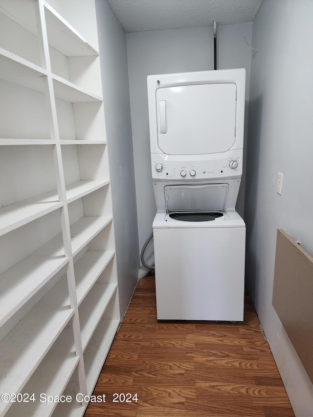 laundry area featuring a textured ceiling, stacked washer / dryer, and dark wood-type flooring