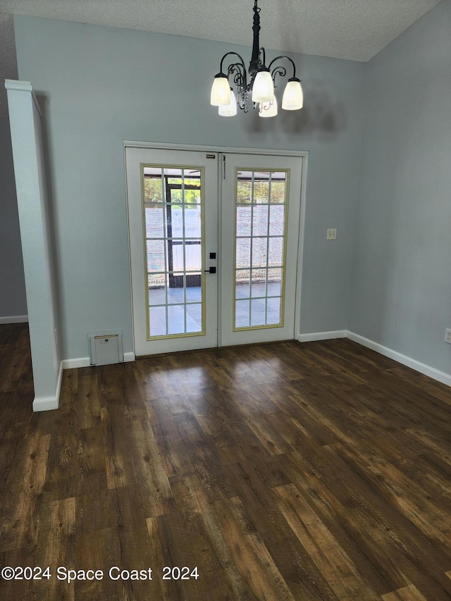 empty room with french doors, an inviting chandelier, a textured ceiling, and dark wood-type flooring