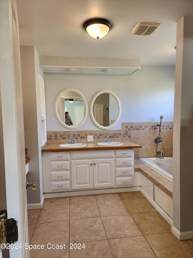 bathroom featuring a relaxing tiled tub, vanity, and tile patterned flooring