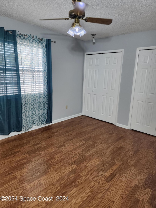 unfurnished bedroom with a textured ceiling, ceiling fan, multiple closets, and hardwood / wood-style flooring