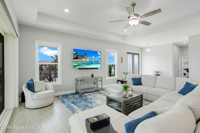 living room with hardwood / wood-style flooring, a raised ceiling, and ceiling fan