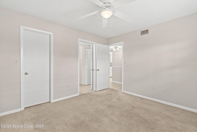 unfurnished bedroom featuring a textured ceiling, ceiling fan, and light colored carpet