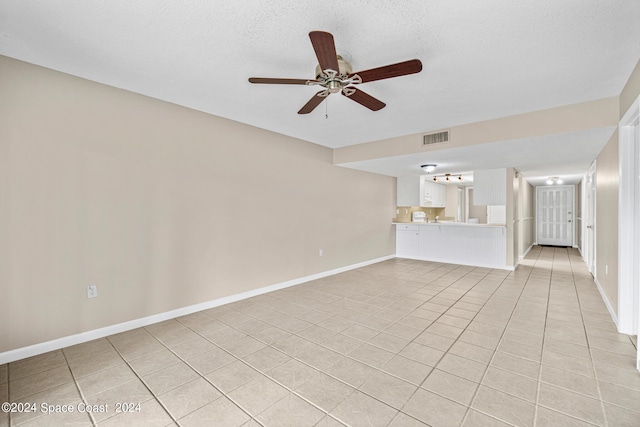 unfurnished living room with ceiling fan, light tile patterned flooring, and a textured ceiling