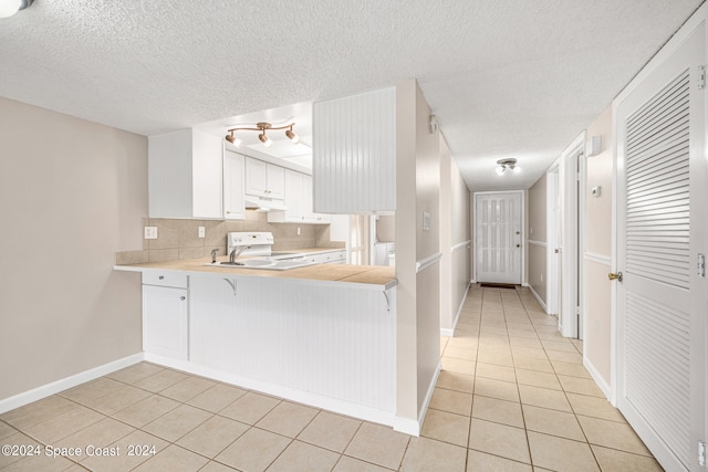 kitchen with a textured ceiling, white cabinetry, kitchen peninsula, white range oven, and light tile patterned floors