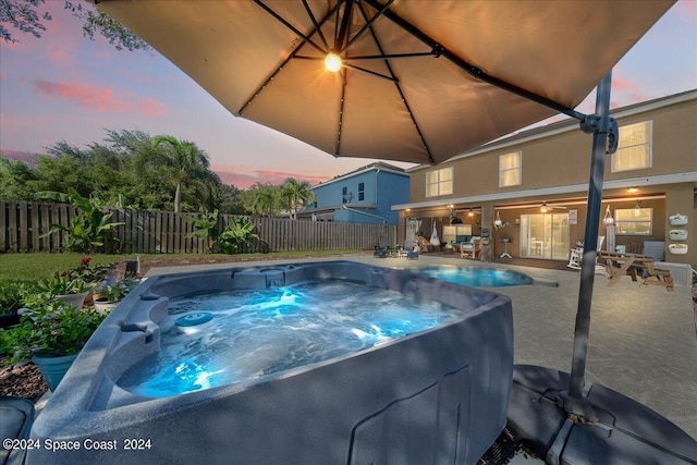 pool at dusk featuring a hot tub and a patio area