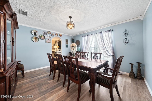 dining area featuring wood-type flooring, a textured ceiling, and crown molding