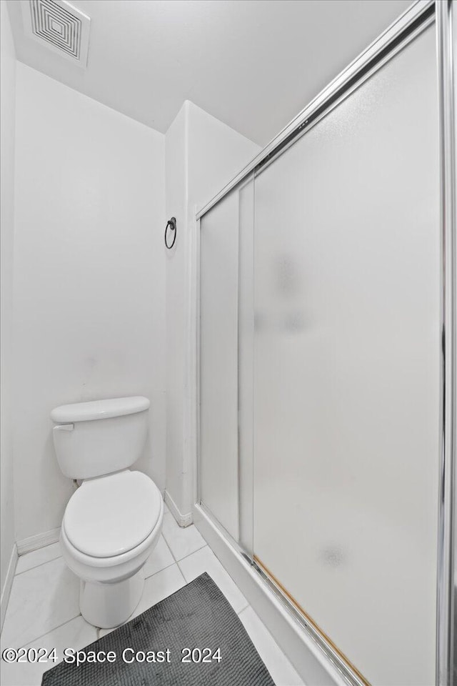 bathroom featuring a shower with shower door, toilet, and tile patterned floors