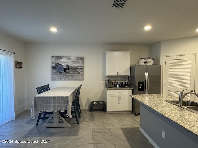 kitchen with white cabinetry, a kitchen breakfast bar, light tile patterned floors, light stone countertops, and stainless steel fridge