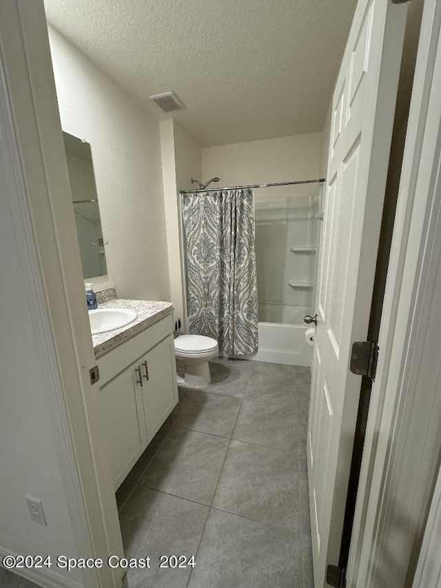 full bathroom with a textured ceiling, tile patterned floors, shower / tub combo with curtain, vanity, and toilet