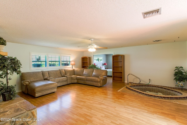 living room with light hardwood / wood-style flooring, ceiling fan, and a textured ceiling