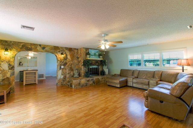 living room featuring ceiling fan, a fireplace, hardwood / wood-style floors, and a textured ceiling