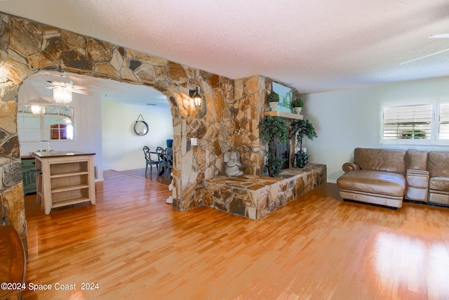 living room with ceiling fan, hardwood / wood-style flooring, a fireplace, and a textured ceiling