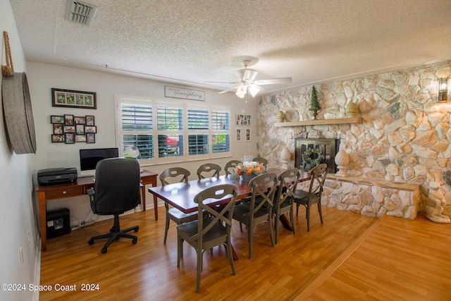 dining room featuring ceiling fan, hardwood / wood-style flooring, a fireplace, and a textured ceiling