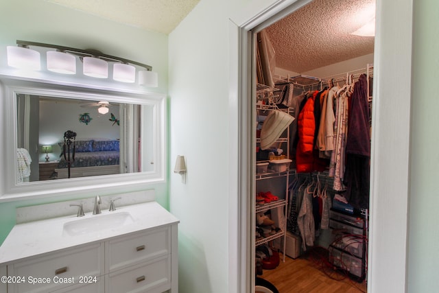 bathroom with ceiling fan, hardwood / wood-style floors, a textured ceiling, and vanity