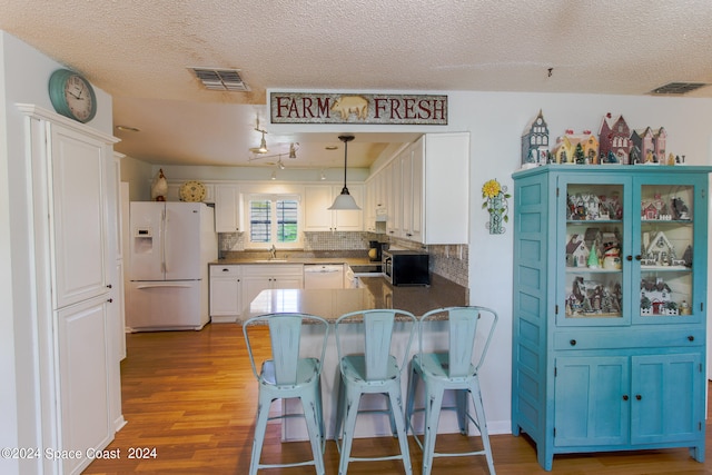 kitchen featuring pendant lighting, white cabinetry, kitchen peninsula, light hardwood / wood-style flooring, and white appliances