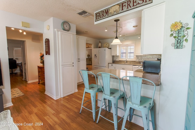 kitchen featuring white cabinets, hanging light fixtures, white appliances, a textured ceiling, and light wood-type flooring