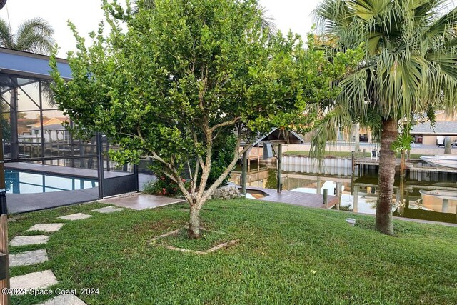 view of yard with a dock, glass enclosure, and a water view