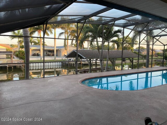 pool at dusk featuring a water view, glass enclosure, and a patio area