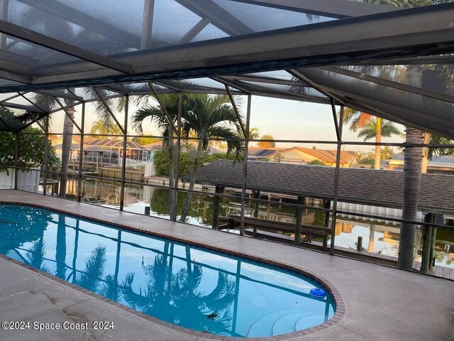 pool at dusk featuring a water view, a lanai, and a patio area