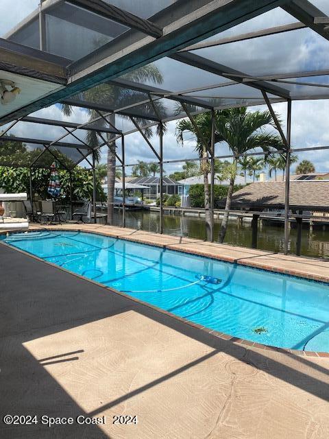 view of swimming pool with a water view, a patio, and glass enclosure