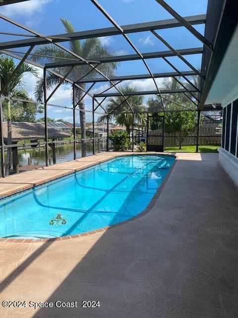 view of pool featuring glass enclosure, a water view, and a patio