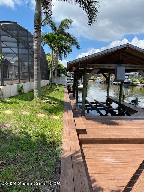 dock area with a lanai, a lawn, and a water view