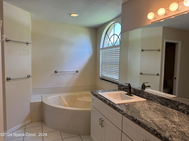 bathroom featuring tile patterned flooring, a textured ceiling, tiled bath, vanity, and toilet