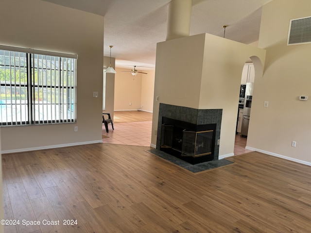 unfurnished living room featuring a textured ceiling, wood-type flooring, a multi sided fireplace, and ceiling fan