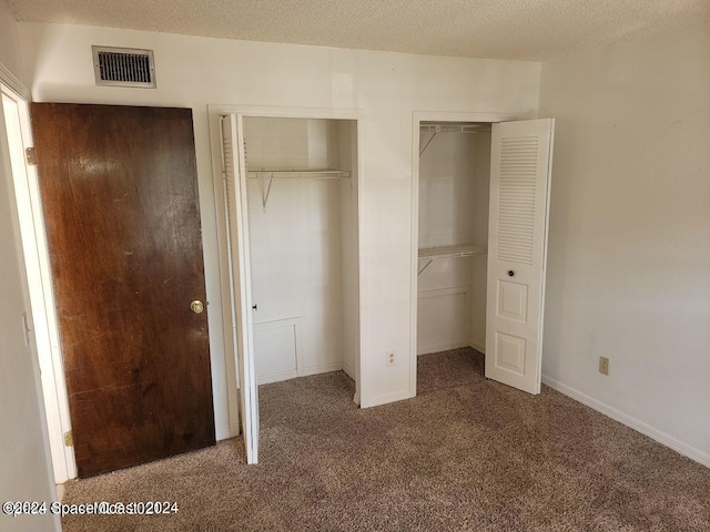 unfurnished bedroom with a textured ceiling, carpet flooring, and multiple closets