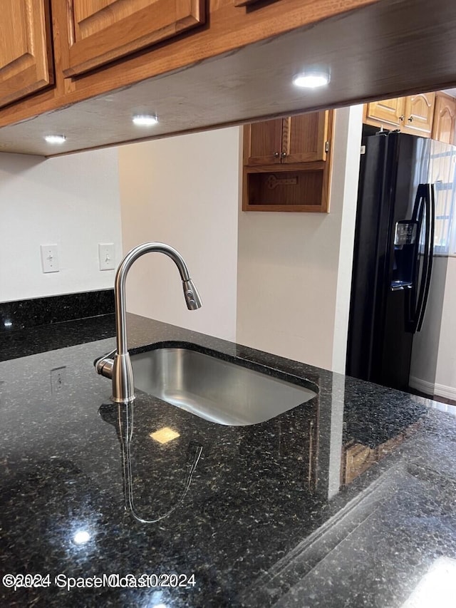 kitchen with black refrigerator with ice dispenser, dark stone countertops, and sink