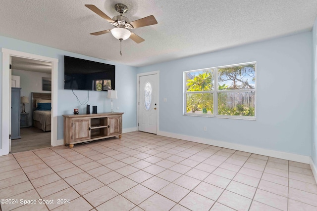 unfurnished living room with a textured ceiling, a fireplace, light tile patterned flooring, and ceiling fan