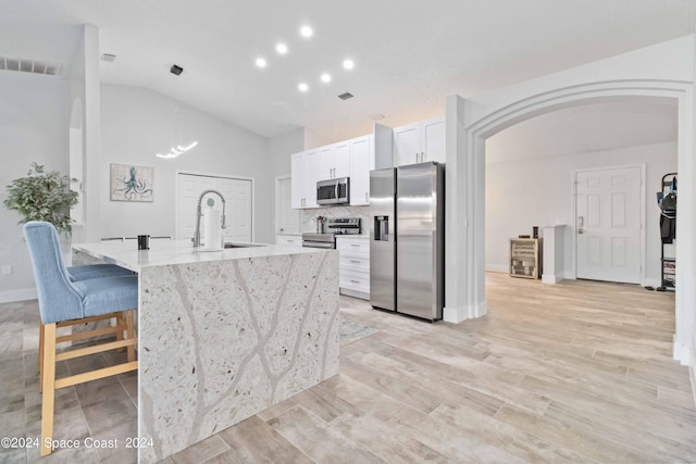 kitchen with white cabinets, vaulted ceiling, appliances with stainless steel finishes, light stone counters, and a breakfast bar area