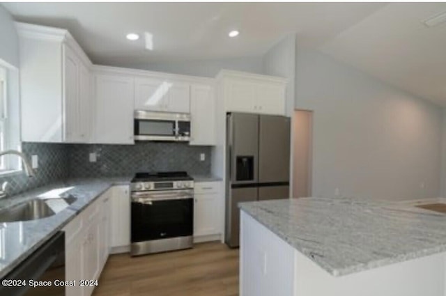 kitchen featuring white cabinets, appliances with stainless steel finishes, vaulted ceiling, and light stone countertops